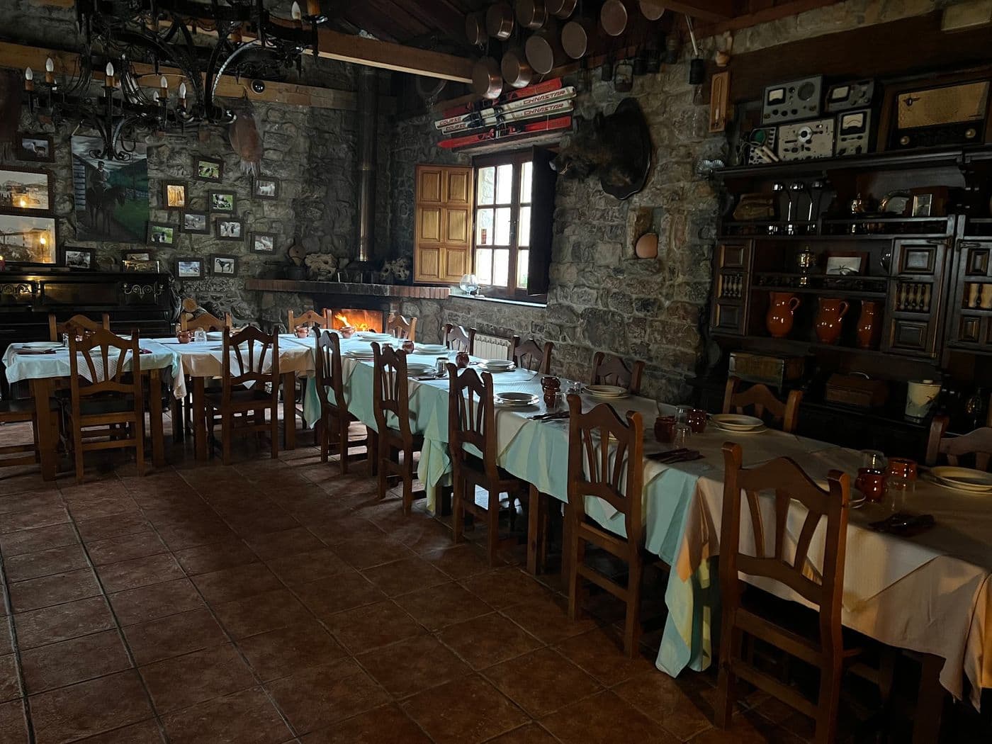 Comedor de La Venta del Aldeano con la chimenea encendida al fondo, las mesas puestas y las cazuelas de cobre colgadas