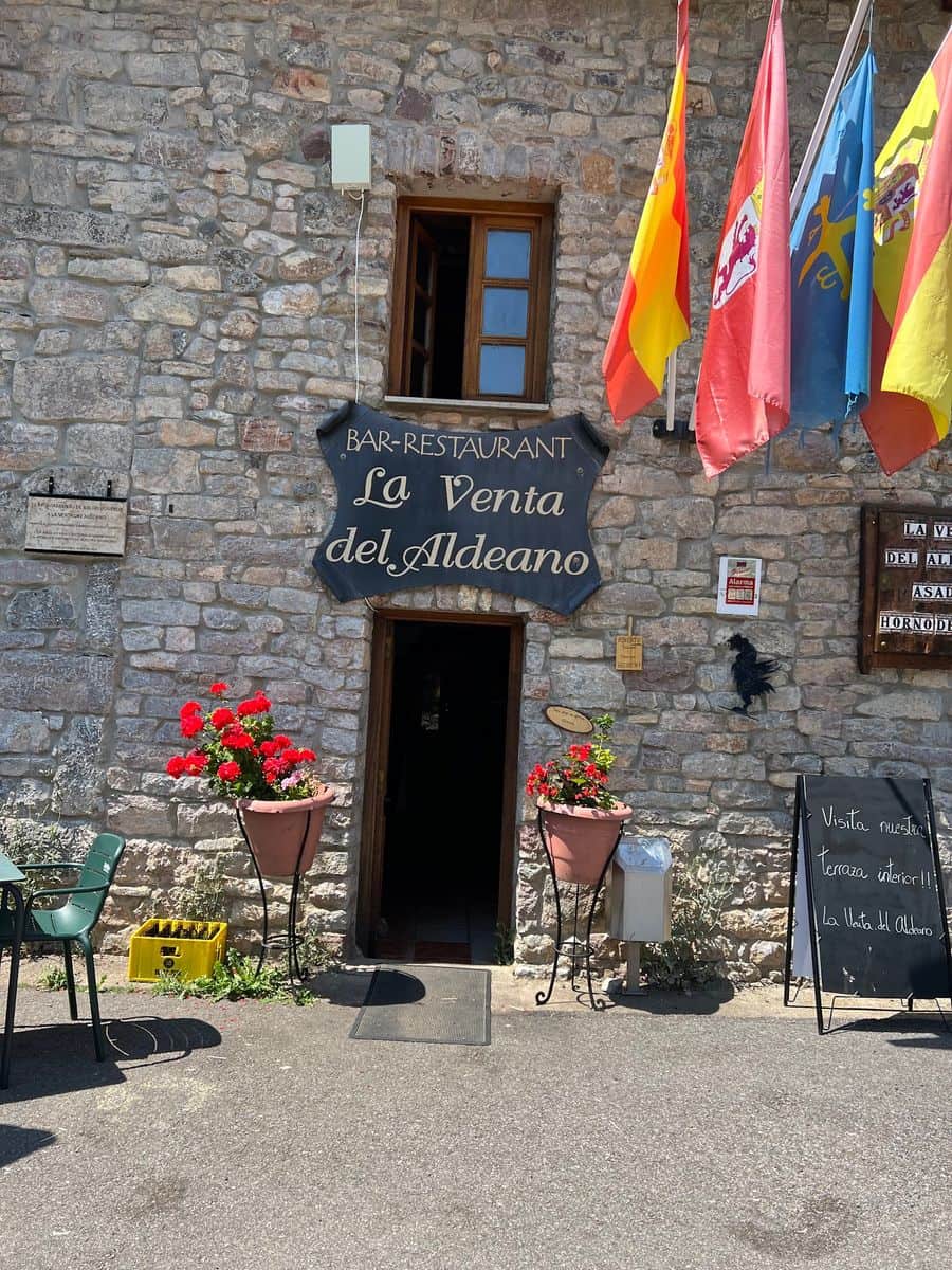 Entrada de La Venta del Aldeano con el rótulo de la casa, los geranios y las banderas