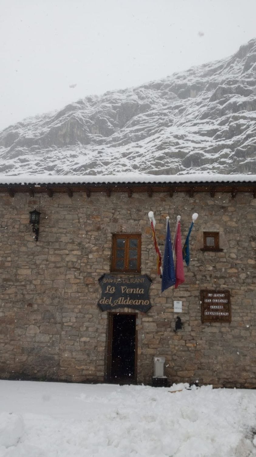 Muro de piedra de La Venta del Aldeano con el cartel de la casa, bajo la nieve